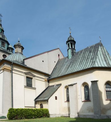 Zdjęcie nr 2: Kościół orientowany, jest budowlą murowaną z cegły i kamienia, na rzucie podłużnym. Korpus trójnawowy i dwuprzęsłowy. Prezbiterium trójprzęsłowe, zamknięte trójbocznie prezbiterium z przylegającymi od północy zakrystią, od południa kruchtą. Na osi kościoła, jednokondygnacyjna, szeroka, przysadzista wieża z kruchtą w przyziemiu i przyległością od zachodu.  Od południa i zachodu, w obrębie pierwszego przęsła naw bocznych jest para kaplic na rzutach zbliżonych do kwadratu. Nawa i prezbiterium przekryte są sklepieniami kolebkowymi z lunetami wspartymi na pilastrach i filarach. Kaplice wieńczą kopuły. Artykulację ścian na zewnątrz prezbiterium stanowi zespół przypór, naroża kaplic ujmują pilastry wpierające obiegający bryłę niepełne belkowanie.
Do wnętrza prowadzi 6 otworów drzwiowych, z czego 2 w kruchcie w wieży ujęte kamiennymi portalami zamkniętymi łukiem koszowym i do kaplicy ujętym kamiennym portalem w formie pary lizen na wysokich cokołach wspierających belkowanie z parą rozet w partii fryzu. Okna korpusu nawowego w kształcie stojących prostokątów, prezbiterium ostrołukowe, natomiast kaplic są prostokątne ujęte kamiennym obramieniem z uszakami w górnych narożach i zwieńczone trójkątnymi przyczółkami. Wieża artykułowana w 2/3 wysokości gzymsem. W dolnej strefie w 3 z 4 ścian po jednym, zamkniętym półkoliście oknie. W górnej partii pośrodku  z czterech po 1 okrągłej tarczy zegara. Wieże wieńczy hełm ujęty 4 latarniami i zwieńczony piątą. Dachy korpusu i prezbiterium dwuspadowe, nad kaplicami kopuły z latarniami, nad zakrystią i kruchtą boczną pulpitowe. Tynki ścian w odcieniach bieli i szarości. 
