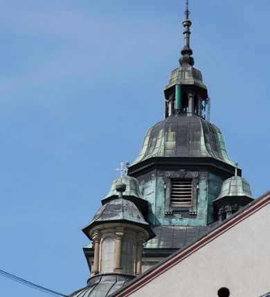 Zdjęcie nr 20: Kościół orientowany, jest budowlą murowaną z cegły i kamienia, na rzucie podłużnym. Korpus trójnawowy i dwuprzęsłowy. Prezbiterium trójprzęsłowe, zamknięte trójbocznie prezbiterium z przylegającymi od północy zakrystią, od południa kruchtą. Na osi kościoła, jednokondygnacyjna, szeroka, przysadzista wieża z kruchtą w przyziemiu i przyległością od zachodu.  Od południa i zachodu, w obrębie pierwszego przęsła naw bocznych jest para kaplic na rzutach zbliżonych do kwadratu. Nawa i prezbiterium przekryte są sklepieniami kolebkowymi z lunetami wspartymi na pilastrach i filarach. Kaplice wieńczą kopuły. Artykulację ścian na zewnątrz prezbiterium stanowi zespół przypór, naroża kaplic ujmują pilastry wpierające obiegający bryłę niepełne belkowanie.
Do wnętrza prowadzi 6 otworów drzwiowych, z czego 2 w kruchcie w wieży ujęte kamiennymi portalami zamkniętymi łukiem koszowym i do kaplicy ujętym kamiennym portalem w formie pary lizen na wysokich cokołach wspierających belkowanie z parą rozet w partii fryzu. Okna korpusu nawowego w kształcie stojących prostokątów, prezbiterium ostrołukowe, natomiast kaplic są prostokątne ujęte kamiennym obramieniem z uszakami w górnych narożach i zwieńczone trójkątnymi przyczółkami. Wieża artykułowana w 2/3 wysokości gzymsem. W dolnej strefie w 3 z 4 ścian po jednym, zamkniętym półkoliście oknie. W górnej partii pośrodku  z czterech po 1 okrągłej tarczy zegara. Wieże wieńczy hełm ujęty 4 latarniami i zwieńczony piątą. Dachy korpusu i prezbiterium dwuspadowe, nad kaplicami kopuły z latarniami, nad zakrystią i kruchtą boczną pulpitowe. Tynki ścian w odcieniach bieli i szarości. 
