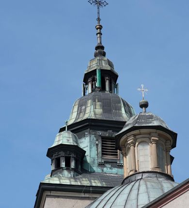 Zdjęcie nr 19: Kościół orientowany, jest budowlą murowaną z cegły i kamienia, na rzucie podłużnym. Korpus trójnawowy i dwuprzęsłowy. Prezbiterium trójprzęsłowe, zamknięte trójbocznie prezbiterium z przylegającymi od północy zakrystią, od południa kruchtą. Na osi kościoła, jednokondygnacyjna, szeroka, przysadzista wieża z kruchtą w przyziemiu i przyległością od zachodu.  Od południa i zachodu, w obrębie pierwszego przęsła naw bocznych jest para kaplic na rzutach zbliżonych do kwadratu. Nawa i prezbiterium przekryte są sklepieniami kolebkowymi z lunetami wspartymi na pilastrach i filarach. Kaplice wieńczą kopuły. Artykulację ścian na zewnątrz prezbiterium stanowi zespół przypór, naroża kaplic ujmują pilastry wpierające obiegający bryłę niepełne belkowanie.
Do wnętrza prowadzi 6 otworów drzwiowych, z czego 2 w kruchcie w wieży ujęte kamiennymi portalami zamkniętymi łukiem koszowym i do kaplicy ujętym kamiennym portalem w formie pary lizen na wysokich cokołach wspierających belkowanie z parą rozet w partii fryzu. Okna korpusu nawowego w kształcie stojących prostokątów, prezbiterium ostrołukowe, natomiast kaplic są prostokątne ujęte kamiennym obramieniem z uszakami w górnych narożach i zwieńczone trójkątnymi przyczółkami. Wieża artykułowana w 2/3 wysokości gzymsem. W dolnej strefie w 3 z 4 ścian po jednym, zamkniętym półkoliście oknie. W górnej partii pośrodku  z czterech po 1 okrągłej tarczy zegara. Wieże wieńczy hełm ujęty 4 latarniami i zwieńczony piątą. Dachy korpusu i prezbiterium dwuspadowe, nad kaplicami kopuły z latarniami, nad zakrystią i kruchtą boczną pulpitowe. Tynki ścian w odcieniach bieli i szarości. 
