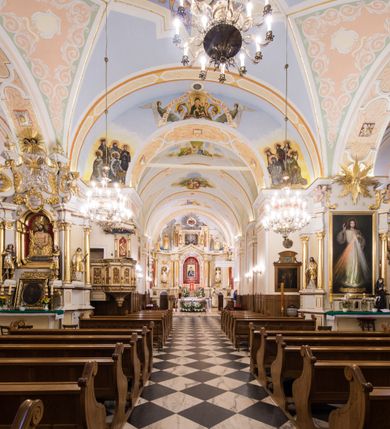 Zdjęcie nr 6: Kościół orientowany, jest budowlą murowaną z cegły i kamienia, na rzucie podłużnym. Korpus trójnawowy i dwuprzęsłowy. Prezbiterium trójprzęsłowe, zamknięte trójbocznie prezbiterium z przylegającymi od północy zakrystią, od południa kruchtą. Na osi kościoła, jednokondygnacyjna, szeroka, przysadzista wieża z kruchtą w przyziemiu i przyległością od zachodu.  Od południa i zachodu, w obrębie pierwszego przęsła naw bocznych jest para kaplic na rzutach zbliżonych do kwadratu. Nawa i prezbiterium przekryte są sklepieniami kolebkowymi z lunetami wspartymi na pilastrach i filarach. Kaplice wieńczą kopuły. Artykulację ścian na zewnątrz prezbiterium stanowi zespół przypór, naroża kaplic ujmują pilastry wpierające obiegający bryłę niepełne belkowanie.
Do wnętrza prowadzi 6 otworów drzwiowych, z czego 2 w kruchcie w wieży ujęte kamiennymi portalami zamkniętymi łukiem koszowym i do kaplicy ujętym kamiennym portalem w formie pary lizen na wysokich cokołach wspierających belkowanie z parą rozet w partii fryzu. Okna korpusu nawowego w kształcie stojących prostokątów, prezbiterium ostrołukowe, natomiast kaplic są prostokątne ujęte kamiennym obramieniem z uszakami w górnych narożach i zwieńczone trójkątnymi przyczółkami. Wieża artykułowana w 2/3 wysokości gzymsem. W dolnej strefie w 3 z 4 ścian po jednym, zamkniętym półkoliście oknie. W górnej partii pośrodku  z czterech po 1 okrągłej tarczy zegara. Wieże wieńczy hełm ujęty 4 latarniami i zwieńczony piątą. Dachy korpusu i prezbiterium dwuspadowe, nad kaplicami kopuły z latarniami, nad zakrystią i kruchtą boczną pulpitowe. Tynki ścian w odcieniach bieli i szarości. 
