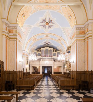 Zdjęcie nr 14: Kościół orientowany, jest budowlą murowaną z cegły i kamienia, na rzucie podłużnym. Korpus trójnawowy i dwuprzęsłowy. Prezbiterium trójprzęsłowe, zamknięte trójbocznie prezbiterium z przylegającymi od północy zakrystią, od południa kruchtą. Na osi kościoła, jednokondygnacyjna, szeroka, przysadzista wieża z kruchtą w przyziemiu i przyległością od zachodu.  Od południa i zachodu, w obrębie pierwszego przęsła naw bocznych jest para kaplic na rzutach zbliżonych do kwadratu. Nawa i prezbiterium przekryte są sklepieniami kolebkowymi z lunetami wspartymi na pilastrach i filarach. Kaplice wieńczą kopuły. Artykulację ścian na zewnątrz prezbiterium stanowi zespół przypór, naroża kaplic ujmują pilastry wpierające obiegający bryłę niepełne belkowanie.
Do wnętrza prowadzi 6 otworów drzwiowych, z czego 2 w kruchcie w wieży ujęte kamiennymi portalami zamkniętymi łukiem koszowym i do kaplicy ujętym kamiennym portalem w formie pary lizen na wysokich cokołach wspierających belkowanie z parą rozet w partii fryzu. Okna korpusu nawowego w kształcie stojących prostokątów, prezbiterium ostrołukowe, natomiast kaplic są prostokątne ujęte kamiennym obramieniem z uszakami w górnych narożach i zwieńczone trójkątnymi przyczółkami. Wieża artykułowana w 2/3 wysokości gzymsem. W dolnej strefie w 3 z 4 ścian po jednym, zamkniętym półkoliście oknie. W górnej partii pośrodku  z czterech po 1 okrągłej tarczy zegara. Wieże wieńczy hełm ujęty 4 latarniami i zwieńczony piątą. Dachy korpusu i prezbiterium dwuspadowe, nad kaplicami kopuły z latarniami, nad zakrystią i kruchtą boczną pulpitowe. Tynki ścian w odcieniach bieli i szarości. 
