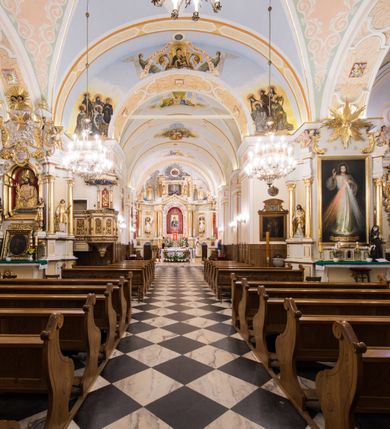 Zdjęcie nr 7: Kościół orientowany, jest budowlą murowaną z cegły i kamienia, na rzucie podłużnym. Korpus trójnawowy i dwuprzęsłowy. Prezbiterium trójprzęsłowe, zamknięte trójbocznie prezbiterium z przylegającymi od północy zakrystią, od południa kruchtą. Na osi kościoła, jednokondygnacyjna, szeroka, przysadzista wieża z kruchtą w przyziemiu i przyległością od zachodu.  Od południa i zachodu, w obrębie pierwszego przęsła naw bocznych jest para kaplic na rzutach zbliżonych do kwadratu. Nawa i prezbiterium przekryte są sklepieniami kolebkowymi z lunetami wspartymi na pilastrach i filarach. Kaplice wieńczą kopuły. Artykulację ścian na zewnątrz prezbiterium stanowi zespół przypór, naroża kaplic ujmują pilastry wpierające obiegający bryłę niepełne belkowanie.
Do wnętrza prowadzi 6 otworów drzwiowych, z czego 2 w kruchcie w wieży ujęte kamiennymi portalami zamkniętymi łukiem koszowym i do kaplicy ujętym kamiennym portalem w formie pary lizen na wysokich cokołach wspierających belkowanie z parą rozet w partii fryzu. Okna korpusu nawowego w kształcie stojących prostokątów, prezbiterium ostrołukowe, natomiast kaplic są prostokątne ujęte kamiennym obramieniem z uszakami w górnych narożach i zwieńczone trójkątnymi przyczółkami. Wieża artykułowana w 2/3 wysokości gzymsem. W dolnej strefie w 3 z 4 ścian po jednym, zamkniętym półkoliście oknie. W górnej partii pośrodku  z czterech po 1 okrągłej tarczy zegara. Wieże wieńczy hełm ujęty 4 latarniami i zwieńczony piątą. Dachy korpusu i prezbiterium dwuspadowe, nad kaplicami kopuły z latarniami, nad zakrystią i kruchtą boczną pulpitowe. Tynki ścian w odcieniach bieli i szarości. 
