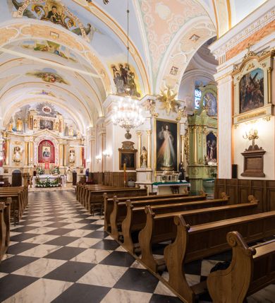 Zdjęcie nr 11: Kościół orientowany, jest budowlą murowaną z cegły i kamienia, na rzucie podłużnym. Korpus trójnawowy i dwuprzęsłowy. Prezbiterium trójprzęsłowe, zamknięte trójbocznie prezbiterium z przylegającymi od północy zakrystią, od południa kruchtą. Na osi kościoła, jednokondygnacyjna, szeroka, przysadzista wieża z kruchtą w przyziemiu i przyległością od zachodu.  Od południa i zachodu, w obrębie pierwszego przęsła naw bocznych jest para kaplic na rzutach zbliżonych do kwadratu. Nawa i prezbiterium przekryte są sklepieniami kolebkowymi z lunetami wspartymi na pilastrach i filarach. Kaplice wieńczą kopuły. Artykulację ścian na zewnątrz prezbiterium stanowi zespół przypór, naroża kaplic ujmują pilastry wpierające obiegający bryłę niepełne belkowanie.
Do wnętrza prowadzi 6 otworów drzwiowych, z czego 2 w kruchcie w wieży ujęte kamiennymi portalami zamkniętymi łukiem koszowym i do kaplicy ujętym kamiennym portalem w formie pary lizen na wysokich cokołach wspierających belkowanie z parą rozet w partii fryzu. Okna korpusu nawowego w kształcie stojących prostokątów, prezbiterium ostrołukowe, natomiast kaplic są prostokątne ujęte kamiennym obramieniem z uszakami w górnych narożach i zwieńczone trójkątnymi przyczółkami. Wieża artykułowana w 2/3 wysokości gzymsem. W dolnej strefie w 3 z 4 ścian po jednym, zamkniętym półkoliście oknie. W górnej partii pośrodku  z czterech po 1 okrągłej tarczy zegara. Wieże wieńczy hełm ujęty 4 latarniami i zwieńczony piątą. Dachy korpusu i prezbiterium dwuspadowe, nad kaplicami kopuły z latarniami, nad zakrystią i kruchtą boczną pulpitowe. Tynki ścian w odcieniach bieli i szarości. 
