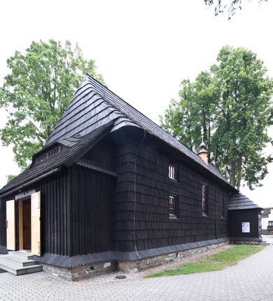 Zdjęcie nr 2: Kościół drewniany, orientowany, o konstrukcji zrębowej, obity gontami. Budowla jednonawowa, z węższym prezbiterium zamkniętym prosto, z zakrystią i kaplicą od strony północnej i kruchtą od południa. Nawa prostokątna, bardzo wydłużona, prezbiterium krótkie, zamknięte prosto. Wszystkie ściany i strony pokrywa polichromia o motywach ornamentalnych i roślinnych otaczających sceny figuralne. Nawa przekryta stropem z zaskrzynieniami, co oznacza, że część konstrukcji dachu, która znajduje się już w przestrzeni nawy została zakryta stropem o skośnym przebiegu, a prezbiterium pozornym stropem kolebkowym. Po prawej stronie dwa duże okna w nawie i jedno w prezbiterium, trzy kolejne w kaplicy. Wejście główne od zachodu, kolejne przez południową kruchtę i do kaplicy, w ścianie zakrystii barokowy portal kamienny z ornamentem roślinnym. Ściany zewnętrzne gładkie, posadowione na niewysokim podmurowaniu zakrytym gontowym fartuchem. Dachy gontowe o konstrukcji więźbowo-zaskrzyniowej. Na kalenicy wieżyczka na sygnaturkę z baniastym hełmem krytym blachą. 