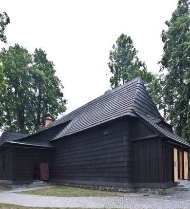 Zdjęcie nr 16: Kościół drewniany, orientowany, o konstrukcji zrębowej, obity gontami. Budowla jednonawowa, z węższym prezbiterium zamkniętym prosto, z zakrystią i kaplicą od strony północnej i kruchtą od południa. Nawa prostokątna, bardzo wydłużona, prezbiterium krótkie, zamknięte prosto. Wszystkie ściany i strony pokrywa polichromia o motywach ornamentalnych i roślinnych otaczających sceny figuralne. Nawa przekryta stropem z zaskrzynieniami, co oznacza, że część konstrukcji dachu, która znajduje się już w przestrzeni nawy została zakryta stropem o skośnym przebiegu, a prezbiterium pozornym stropem kolebkowym. Po prawej stronie dwa duże okna w nawie i jedno w prezbiterium, trzy kolejne w kaplicy. Wejście główne od zachodu, kolejne przez południową kruchtę i do kaplicy, w ścianie zakrystii barokowy portal kamienny z ornamentem roślinnym. Ściany zewnętrzne gładkie, posadowione na niewysokim podmurowaniu zakrytym gontowym fartuchem. Dachy gontowe o konstrukcji więźbowo-zaskrzyniowej. Na kalenicy wieżyczka na sygnaturkę z baniastym hełmem krytym blachą. 