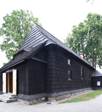 Zdjęcie nr 1: Kościół drewniany, orientowany, o konstrukcji zrębowej, obity gontami. Budowla jednonawowa, z węższym prezbiterium zamkniętym prosto, z zakrystią i kaplicą od strony północnej i kruchtą od południa. Nawa prostokątna, bardzo wydłużona, prezbiterium krótkie, zamknięte prosto. Wszystkie ściany i strony pokrywa polichromia o motywach ornamentalnych i roślinnych otaczających sceny figuralne. Nawa przekryta stropem z zaskrzynieniami, co oznacza, że część konstrukcji dachu, która znajduje się już w przestrzeni nawy została zakryta stropem o skośnym przebiegu, a prezbiterium pozornym stropem kolebkowym. Po prawej stronie dwa duże okna w nawie i jedno w prezbiterium, trzy kolejne w kaplicy. Wejście główne od zachodu, kolejne przez południową kruchtę i do kaplicy, w ścianie zakrystii barokowy portal kamienny z ornamentem roślinnym. Ściany zewnętrzne gładkie, posadowione na niewysokim podmurowaniu zakrytym gontowym fartuchem. Dachy gontowe o konstrukcji więźbowo-zaskrzyniowej. Na kalenicy wieżyczka na sygnaturkę z baniastym hełmem krytym blachą. 