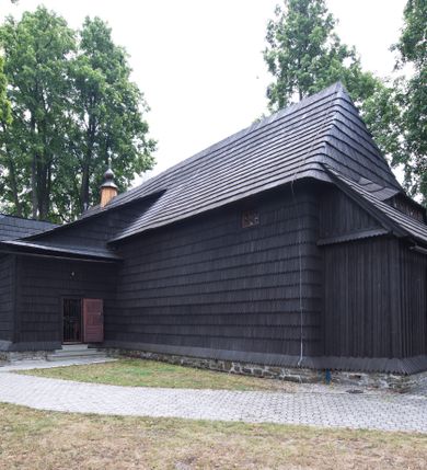 Zdjęcie nr 17: Kościół drewniany, orientowany, o konstrukcji zrębowej, obity gontami. Budowla jednonawowa, z węższym prezbiterium zamkniętym prosto, z zakrystią i kaplicą od strony północnej i kruchtą od południa. Nawa prostokątna, bardzo wydłużona, prezbiterium krótkie, zamknięte prosto. Wszystkie ściany i strony pokrywa polichromia o motywach ornamentalnych i roślinnych otaczających sceny figuralne. Nawa przekryta stropem z zaskrzynieniami, co oznacza, że część konstrukcji dachu, która znajduje się już w przestrzeni nawy została zakryta stropem o skośnym przebiegu, a prezbiterium pozornym stropem kolebkowym. Po prawej stronie dwa duże okna w nawie i jedno w prezbiterium, trzy kolejne w kaplicy. Wejście główne od zachodu, kolejne przez południową kruchtę i do kaplicy, w ścianie zakrystii barokowy portal kamienny z ornamentem roślinnym. Ściany zewnętrzne gładkie, posadowione na niewysokim podmurowaniu zakrytym gontowym fartuchem. Dachy gontowe o konstrukcji więźbowo-zaskrzyniowej. Na kalenicy wieżyczka na sygnaturkę z baniastym hełmem krytym blachą. 