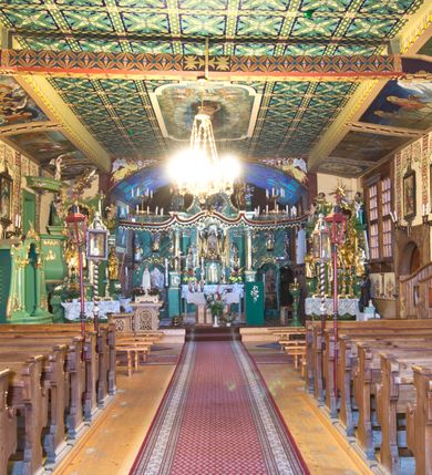 Zdjęcie nr 3: Kościół drewniany, orientowany, o konstrukcji zrębowej, obity gontami. Budowla jednonawowa, z węższym prezbiterium zamkniętym prosto, z zakrystią i kaplicą od strony północnej i kruchtą od południa. Nawa prostokątna, bardzo wydłużona, prezbiterium krótkie, zamknięte prosto. Wszystkie ściany i strony pokrywa polichromia o motywach ornamentalnych i roślinnych otaczających sceny figuralne. Nawa przekryta stropem z zaskrzynieniami, co oznacza, że część konstrukcji dachu, która znajduje się już w przestrzeni nawy została zakryta stropem o skośnym przebiegu, a prezbiterium pozornym stropem kolebkowym. Po prawej stronie dwa duże okna w nawie i jedno w prezbiterium, trzy kolejne w kaplicy. Wejście główne od zachodu, kolejne przez południową kruchtę i do kaplicy, w ścianie zakrystii barokowy portal kamienny z ornamentem roślinnym. Ściany zewnętrzne gładkie, posadowione na niewysokim podmurowaniu zakrytym gontowym fartuchem. Dachy gontowe o konstrukcji więźbowo-zaskrzyniowej. Na kalenicy wieżyczka na sygnaturkę z baniastym hełmem krytym blachą. 