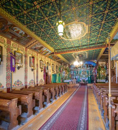 Zdjęcie nr 5: Kościół drewniany, orientowany, o konstrukcji zrębowej, obity gontami. Budowla jednonawowa, z węższym prezbiterium zamkniętym prosto, z zakrystią i kaplicą od strony północnej i kruchtą od południa. Nawa prostokątna, bardzo wydłużona, prezbiterium krótkie, zamknięte prosto. Wszystkie ściany i strony pokrywa polichromia o motywach ornamentalnych i roślinnych otaczających sceny figuralne. Nawa przekryta stropem z zaskrzynieniami, co oznacza, że część konstrukcji dachu, która znajduje się już w przestrzeni nawy została zakryta stropem o skośnym przebiegu, a prezbiterium pozornym stropem kolebkowym. Po prawej stronie dwa duże okna w nawie i jedno w prezbiterium, trzy kolejne w kaplicy. Wejście główne od zachodu, kolejne przez południową kruchtę i do kaplicy, w ścianie zakrystii barokowy portal kamienny z ornamentem roślinnym. Ściany zewnętrzne gładkie, posadowione na niewysokim podmurowaniu zakrytym gontowym fartuchem. Dachy gontowe o konstrukcji więźbowo-zaskrzyniowej. Na kalenicy wieżyczka na sygnaturkę z baniastym hełmem krytym blachą. 