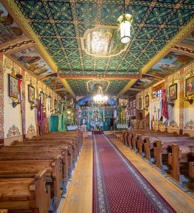 Zdjęcie nr 4: Kościół drewniany, orientowany, o konstrukcji zrębowej, obity gontami. Budowla jednonawowa, z węższym prezbiterium zamkniętym prosto, z zakrystią i kaplicą od strony północnej i kruchtą od południa. Nawa prostokątna, bardzo wydłużona, prezbiterium krótkie, zamknięte prosto. Wszystkie ściany i strony pokrywa polichromia o motywach ornamentalnych i roślinnych otaczających sceny figuralne. Nawa przekryta stropem z zaskrzynieniami, co oznacza, że część konstrukcji dachu, która znajduje się już w przestrzeni nawy została zakryta stropem o skośnym przebiegu, a prezbiterium pozornym stropem kolebkowym. Po prawej stronie dwa duże okna w nawie i jedno w prezbiterium, trzy kolejne w kaplicy. Wejście główne od zachodu, kolejne przez południową kruchtę i do kaplicy, w ścianie zakrystii barokowy portal kamienny z ornamentem roślinnym. Ściany zewnętrzne gładkie, posadowione na niewysokim podmurowaniu zakrytym gontowym fartuchem. Dachy gontowe o konstrukcji więźbowo-zaskrzyniowej. Na kalenicy wieżyczka na sygnaturkę z baniastym hełmem krytym blachą. 