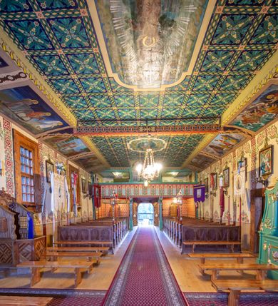 Zdjęcie nr 8: Kościół drewniany, orientowany, o konstrukcji zrębowej, obity gontami. Budowla jednonawowa, z węższym prezbiterium zamkniętym prosto, z zakrystią i kaplicą od strony północnej i kruchtą od południa. Nawa prostokątna, bardzo wydłużona, prezbiterium krótkie, zamknięte prosto. Wszystkie ściany i strony pokrywa polichromia o motywach ornamentalnych i roślinnych otaczających sceny figuralne. Nawa przekryta stropem z zaskrzynieniami, co oznacza, że część konstrukcji dachu, która znajduje się już w przestrzeni nawy została zakryta stropem o skośnym przebiegu, a prezbiterium pozornym stropem kolebkowym. Po prawej stronie dwa duże okna w nawie i jedno w prezbiterium, trzy kolejne w kaplicy. Wejście główne od zachodu, kolejne przez południową kruchtę i do kaplicy, w ścianie zakrystii barokowy portal kamienny z ornamentem roślinnym. Ściany zewnętrzne gładkie, posadowione na niewysokim podmurowaniu zakrytym gontowym fartuchem. Dachy gontowe o konstrukcji więźbowo-zaskrzyniowej. Na kalenicy wieżyczka na sygnaturkę z baniastym hełmem krytym blachą. 