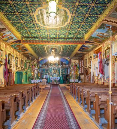 Zdjęcie nr 22: Kościół drewniany, orientowany, o konstrukcji zrębowej, obity gontami. Budowla jednonawowa, z węższym prezbiterium zamkniętym prosto, z zakrystią i kaplicą od strony północnej i kruchtą od południa. Nawa prostokątna, bardzo wydłużona, prezbiterium krótkie, zamknięte prosto. Wszystkie ściany i strony pokrywa polichromia o motywach ornamentalnych i roślinnych otaczających sceny figuralne. Nawa przekryta stropem z zaskrzynieniami, co oznacza, że część konstrukcji dachu, która znajduje się już w przestrzeni nawy została zakryta stropem o skośnym przebiegu, a prezbiterium pozornym stropem kolebkowym. Po prawej stronie dwa duże okna w nawie i jedno w prezbiterium, trzy kolejne w kaplicy. Wejście główne od zachodu, kolejne przez południową kruchtę i do kaplicy, w ścianie zakrystii barokowy portal kamienny z ornamentem roślinnym. Ściany zewnętrzne gładkie, posadowione na niewysokim podmurowaniu zakrytym gontowym fartuchem. Dachy gontowe o konstrukcji więźbowo-zaskrzyniowej. Na kalenicy wieżyczka na sygnaturkę z baniastym hełmem krytym blachą. 