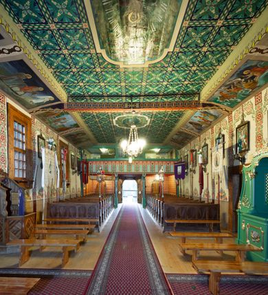 Zdjęcie nr 9: Kościół drewniany, orientowany, o konstrukcji zrębowej, obity gontami. Budowla jednonawowa, z węższym prezbiterium zamkniętym prosto, z zakrystią i kaplicą od strony północnej i kruchtą od południa. Nawa prostokątna, bardzo wydłużona, prezbiterium krótkie, zamknięte prosto. Wszystkie ściany i strony pokrywa polichromia o motywach ornamentalnych i roślinnych otaczających sceny figuralne. Nawa przekryta stropem z zaskrzynieniami, co oznacza, że część konstrukcji dachu, która znajduje się już w przestrzeni nawy została zakryta stropem o skośnym przebiegu, a prezbiterium pozornym stropem kolebkowym. Po prawej stronie dwa duże okna w nawie i jedno w prezbiterium, trzy kolejne w kaplicy. Wejście główne od zachodu, kolejne przez południową kruchtę i do kaplicy, w ścianie zakrystii barokowy portal kamienny z ornamentem roślinnym. Ściany zewnętrzne gładkie, posadowione na niewysokim podmurowaniu zakrytym gontowym fartuchem. Dachy gontowe o konstrukcji więźbowo-zaskrzyniowej. Na kalenicy wieżyczka na sygnaturkę z baniastym hełmem krytym blachą. 