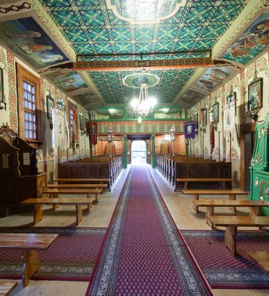 Zdjęcie nr 15: Kościół drewniany, orientowany, o konstrukcji zrębowej, obity gontami. Budowla jednonawowa, z węższym prezbiterium zamkniętym prosto, z zakrystią i kaplicą od strony północnej i kruchtą od południa. Nawa prostokątna, bardzo wydłużona, prezbiterium krótkie, zamknięte prosto. Wszystkie ściany i strony pokrywa polichromia o motywach ornamentalnych i roślinnych otaczających sceny figuralne. Nawa przekryta stropem z zaskrzynieniami, co oznacza, że część konstrukcji dachu, która znajduje się już w przestrzeni nawy została zakryta stropem o skośnym przebiegu, a prezbiterium pozornym stropem kolebkowym. Po prawej stronie dwa duże okna w nawie i jedno w prezbiterium, trzy kolejne w kaplicy. Wejście główne od zachodu, kolejne przez południową kruchtę i do kaplicy, w ścianie zakrystii barokowy portal kamienny z ornamentem roślinnym. Ściany zewnętrzne gładkie, posadowione na niewysokim podmurowaniu zakrytym gontowym fartuchem. Dachy gontowe o konstrukcji więźbowo-zaskrzyniowej. Na kalenicy wieżyczka na sygnaturkę z baniastym hełmem krytym blachą. 