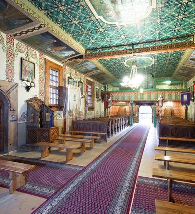 Zdjęcie nr 12: Kościół drewniany, orientowany, o konstrukcji zrębowej, obity gontami. Budowla jednonawowa, z węższym prezbiterium zamkniętym prosto, z zakrystią i kaplicą od strony północnej i kruchtą od południa. Nawa prostokątna, bardzo wydłużona, prezbiterium krótkie, zamknięte prosto. Wszystkie ściany i strony pokrywa polichromia o motywach ornamentalnych i roślinnych otaczających sceny figuralne. Nawa przekryta stropem z zaskrzynieniami, co oznacza, że część konstrukcji dachu, która znajduje się już w przestrzeni nawy została zakryta stropem o skośnym przebiegu, a prezbiterium pozornym stropem kolebkowym. Po prawej stronie dwa duże okna w nawie i jedno w prezbiterium, trzy kolejne w kaplicy. Wejście główne od zachodu, kolejne przez południową kruchtę i do kaplicy, w ścianie zakrystii barokowy portal kamienny z ornamentem roślinnym. Ściany zewnętrzne gładkie, posadowione na niewysokim podmurowaniu zakrytym gontowym fartuchem. Dachy gontowe o konstrukcji więźbowo-zaskrzyniowej. Na kalenicy wieżyczka na sygnaturkę z baniastym hełmem krytym blachą. 