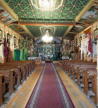 Zdjęcie nr 20: Kościół drewniany, orientowany, o konstrukcji zrębowej, obity gontami. Budowla jednonawowa, z węższym prezbiterium zamkniętym prosto, z zakrystią i kaplicą od strony północnej i kruchtą od południa. Nawa prostokątna, bardzo wydłużona, prezbiterium krótkie, zamknięte prosto. Wszystkie ściany i strony pokrywa polichromia o motywach ornamentalnych i roślinnych otaczających sceny figuralne. Nawa przekryta stropem z zaskrzynieniami, co oznacza, że część konstrukcji dachu, która znajduje się już w przestrzeni nawy została zakryta stropem o skośnym przebiegu, a prezbiterium pozornym stropem kolebkowym. Po prawej stronie dwa duże okna w nawie i jedno w prezbiterium, trzy kolejne w kaplicy. Wejście główne od zachodu, kolejne przez południową kruchtę i do kaplicy, w ścianie zakrystii barokowy portal kamienny z ornamentem roślinnym. Ściany zewnętrzne gładkie, posadowione na niewysokim podmurowaniu zakrytym gontowym fartuchem. Dachy gontowe o konstrukcji więźbowo-zaskrzyniowej. Na kalenicy wieżyczka na sygnaturkę z baniastym hełmem krytym blachą. 