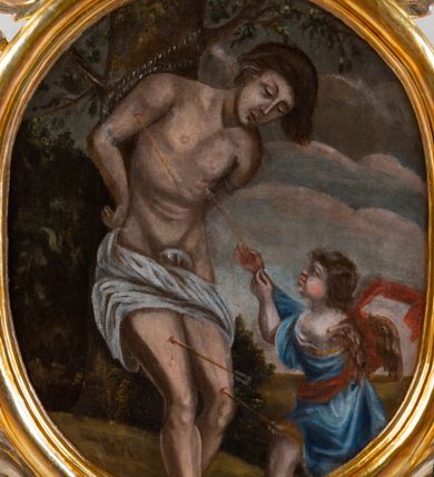 Zdjęcie nr 4: Feretron dwustronny z przedstawieniem Matki Bożej i św. Sebastiana. Na profilowanym postumencie zaopatrzonym w otwory na drążki do noszenia, dołem puklowanym, została umieszczona dwustronnie rzeźbiona, owalna rama utworzona z liści schnącego akantu, z dwoma aniołkami podtrzymującymi koronę w zwieńczeniu. Aniołki ukazano frontalnie, z jedną ręką złożoną na brzuchu, drugą wyprostowaną, podtrzymującą koronę w typie zamkniętym, ze złożonymi skrzydłami, z przepaską na biodrach utworzoną z liści akantu. Mają jasną karnację, szerokie twarze, zarumienione policzki, drobne, czerwone usta oraz krótkie, szerokie nosy. Włosy ciemnobrązowe, średniej długości, z przedziałkiem na środku. Na awersie znajduje się obraz z wizerunkiem popiersia Matki Bożej w owalnej ramie utworzonej z liści przewiązanych w czterech miejscach karbowaną wstęgą. Maria ukazana frontalnie, z głową delikatnie przechyloną w dół i zwróconą w prawo, z rękami złożonymi na piersi. Ubrana jest w białą suknię z długimi rękawami i niebieski płaszcz zarzucony na ramiona. Na głowie ma białą chustę i niebieski welon. Włosy długie, z przedziałkiem na środku, falowane. Dłonie subtelne, z długimi palcami, karnacja jasna, drobne usta, przymknięte powieki, długi, wąski nos. Wokół głowy Marii namalowano 11 gwiazd. Tło obrazu jasnożółte. Na rewersie obraz z przedstawieniem św. Sebastiana w owalnej, profilowanej, wypukłej ramie. W centrum kompozycji postać męczennika przywiązanego do drzewa. Jest zwrócony w trzech czwartych w lewo, delikatnie pochylony, z nogami ugiętymi w kolanach, rękami związanymi z tyłu. Ciało przebite czterema strzałami tkwiącymi w prawym ramieniu, lewym boku i obydwu nogach. Twarz podłużna z długim, wąskim nosem. U dołu po prawej aniołek, wysokością sięgający do połowy św. Sebastiana, ukazany z lewego profilu, wyciągający strzałę z boku świętego. Aniołek jest ubrany w niebieską szatę do kolan oraz czerwoną chustę zwiewnie unoszącą się ponad plecami. Ma twarz okrągłą, z wysuniętym podbródkiem, duże, szerokie usta, krótki, wąski nos, włosy średniej długości. W tle, po lewej stronie roślinność, po prawej błękitne niebo. Polichromia podstawy w kolorze brązowym i zielonym, rama i detale złocone i srebrzone.