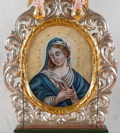 Zdjęcie nr 1: Feretron dwustronny z przedstawieniem Matki Bożej i św. Sebastiana. Na profilowanym postumencie zaopatrzonym w otwory na drążki do noszenia, dołem puklowanym, została umieszczona dwustronnie rzeźbiona, owalna rama utworzona z liści schnącego akantu, z dwoma aniołkami podtrzymującymi koronę w zwieńczeniu. Aniołki ukazano frontalnie, z jedną ręką złożoną na brzuchu, drugą wyprostowaną, podtrzymującą koronę w typie zamkniętym, ze złożonymi skrzydłami, z przepaską na biodrach utworzoną z liści akantu. Mają jasną karnację, szerokie twarze, zarumienione policzki, drobne, czerwone usta oraz krótkie, szerokie nosy. Włosy ciemnobrązowe, średniej długości, z przedziałkiem na środku. Na awersie znajduje się obraz z wizerunkiem popiersia Matki Bożej w owalnej ramie utworzonej z liści przewiązanych w czterech miejscach karbowaną wstęgą. Maria ukazana frontalnie, z głową delikatnie przechyloną w dół i zwróconą w prawo, z rękami złożonymi na piersi. Ubrana jest w białą suknię z długimi rękawami i niebieski płaszcz zarzucony na ramiona. Na głowie ma białą chustę i niebieski welon. Włosy długie, z przedziałkiem na środku, falowane. Dłonie subtelne, z długimi palcami, karnacja jasna, drobne usta, przymknięte powieki, długi, wąski nos. Wokół głowy Marii namalowano 11 gwiazd. Tło obrazu jasnożółte. Na rewersie obraz z przedstawieniem św. Sebastiana w owalnej, profilowanej, wypukłej ramie. W centrum kompozycji postać męczennika przywiązanego do drzewa. Jest zwrócony w trzech czwartych w lewo, delikatnie pochylony, z nogami ugiętymi w kolanach, rękami związanymi z tyłu. Ciało przebite czterema strzałami tkwiącymi w prawym ramieniu, lewym boku i obydwu nogach. Twarz podłużna z długim, wąskim nosem. U dołu po prawej aniołek, wysokością sięgający do połowy św. Sebastiana, ukazany z lewego profilu, wyciągający strzałę z boku świętego. Aniołek jest ubrany w niebieską szatę do kolan oraz czerwoną chustę zwiewnie unoszącą się ponad plecami. Ma twarz okrągłą, z wysuniętym podbródkiem, duże, szerokie usta, krótki, wąski nos, włosy średniej długości. W tle, po lewej stronie roślinność, po prawej błękitne niebo. Polichromia podstawy w kolorze brązowym i zielonym, rama i detale złocone i srebrzone.