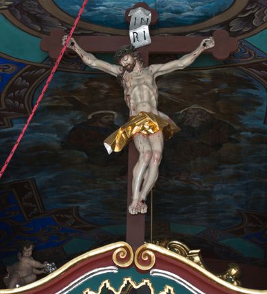 Zdjęcie nr 1: Rzeźby ukrzyżowanego Jezusa, Matki Boskiej oraz św. Jana Ewangelisty tworzące grupę Ukrzyżowania. W centrum kompozycji krzyż o trójlistnym zakończeniu ramion, na nim figura Chrystusa w typie Christo morte, przybita do krzyża trzema gwoździami. Ciało w delikatnym zwisie o stosunkowo szeroko rozłożonych ramionach, esowato wygięte, kolana zgięte, stopy w układzie prawa na lewą, głowa opada na prawy bark. Jezus ma szczupłą twarz, okoloną krótkim zarostem oraz długimi, silnie skręconymi włosami opadającymi na plecy i prawe ramię; na głowie gruba, zielona korona cierniowa. Ciało silnie wychudzone o wyraźnie podkreślonej muskulaturze oraz zapadniętej klatce piersiowej z zaznaczoną linią żeber oraz mostka. Przez biodra przewiązane krótkim, złotym perizonium zawiązanym w partii podbrzusza, z fragmentami tkaniny rozwianymi na boki, draperia silnie łamana. 
Po lewej stronie krzyża figura Matki Boskiej, zwrócona w stronę Ukrzyżowanego. Maria stoi w kontrapoście, ma esowato wygięto sylwetkę i głowę uniesioną do góry. Jej lewa ręka spoczywa na piersi, prawą wyciąga przed siebie. Ma pełną twarz, o wystającym podbródku. Ubrana jest w czerwoną suknię o wywiniętych mankietach oraz okalający jej ciało niebieski płaszcz; na głowie ma biały welon. 
Po prawej stronie figura św. Jana ukazanego w skręcie, z rękami złożonymi  po lewej stronie ciała i z głową skierowaną w prawo. Święty stoi w kontrapoście, z prawym biodrem mocno wypchniętym do boku. Ma prostokątną twarz z półprzymkniętymi, migdałowatymi oczami, dużym nosem i mocno zarysowanymi ustami, wzrok kieruje w dół. Na plecy i ramiona opadają mu silnie skręcone, długie włosy. Jest ubrany w laserowaną zieloną suknię z żółtym podbiciem, silnie przylegającą do ciała i marszczoną oraz czerwony płaszcz przerzucony przez lewe ramię, opadający na lewy bok i plecy. Polichromia naturalistyczna w odsłoniętych partiach ciała. 