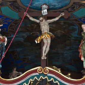 Zdjęcie nr 1: Rzeźby ukrzyżowanego Jezusa, Matki Boskiej oraz św. Jana Ewangelisty tworzące grupę Ukrzyżowania. W centrum kompozycji krzyż o trójlistnym zakończeniu ramion, na nim figura Chrystusa w typie Christo morte, przybita do krzyża trzema gwoździami. Ciało w delikatnym zwisie o stosunkowo szeroko rozłożonych ramionach, esowato wygięte, kolana zgięte, stopy w układzie prawa na lewą, głowa opada na prawy bark. Jezus ma szczupłą twarz, okoloną krótkim zarostem oraz długimi, silnie skręconymi włosami opadającymi na plecy i prawe ramię; na głowie gruba, zielona korona cierniowa. Ciało silnie wychudzone o wyraźnie podkreślonej muskulaturze oraz zapadniętej klatce piersiowej z zaznaczoną linią żeber oraz mostka. Przez biodra przewiązane krótkim, złotym perizonium zawiązanym w partii podbrzusza, z fragmentami tkaniny rozwianymi na boki, draperia silnie łamana. 
Po lewej stronie krzyża figura Matki Boskiej, zwrócona w stronę Ukrzyżowanego. Maria stoi w kontrapoście, ma esowato wygięto sylwetkę i głowę uniesioną do góry. Jej lewa ręka spoczywa na piersi, prawą wyciąga przed siebie. Ma pełną twarz, o wystającym podbródku. Ubrana jest w czerwoną suknię o wywiniętych mankietach oraz okalający jej ciało niebieski płaszcz; na głowie ma biały welon. 
Po prawej stronie figura św. Jana ukazanego w skręcie, z rękami złożonymi  po lewej stronie ciała i z głową skierowaną w prawo. Święty stoi w kontrapoście, z prawym biodrem mocno wypchniętym do boku. Ma prostokątną twarz z półprzymkniętymi, migdałowatymi oczami, dużym nosem i mocno zarysowanymi ustami, wzrok kieruje w dół. Na plecy i ramiona opadają mu silnie skręcone, długie włosy. Jest ubrany w laserowaną zieloną suknię z żółtym podbiciem, silnie przylegającą do ciała i marszczoną oraz czerwony płaszcz przerzucony przez lewe ramię, opadający na lewy bok i plecy. Polichromia naturalistyczna w odsłoniętych partiach ciała. 