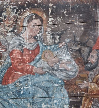 Zdjęcie nr 2: Obraz w formie leżącego prostokąta ze sceną pokłonu trzech króli. Z lewej strony kompozycji siedzi Maria prezentująca Dzieciątko klęczącemu przed nią królowi. Jest ubrana w czerwoną suknię i niebieski płaszcz, który obszernymi fałdami okrywa jej nogi i plecy. Na głowie ma welon, wokół głowy nimb. Ma owalną, smutną twarz, niewielkie oczy i usta, spod welonu widać ciemne, zaczesane na boki włosy. Za nią stoi św. Józef z siwą brodą i włosami, ubrany w jasną suknię i brązowy płaszcz. Za ich plecami widać nakrytą strzechą stajnię ze zwierzętami. Klęczący przed Marią król prezentuje otwartą szkatułkę ze złotem. Ma podłużną twarz, siwe włosy i brodę, żółty płaszcz. Za nim stoi drugi, trzymający łódkę z kadzidłem. Jest ubrany w białą tunikę i czerwony płaszcz, na głowie ma otwartą koronę, w uszach złote kolczyki. Obok niego ostatni władca trzyma w rękach pojemnik z mirrą. Jest ubrany w bardzo obszerny, zdobiony ornamentami płaszcz, turban i otwartą koronę. Za sceną, z tyłu po prawej stronie widać architekturę miasta otoczonego murami, a za nim rozmyte wzgórza. W prawym dolnym rogu krzak wyrastający zza kamienia. W partii nieba widoczna gwiazda betlejemska. 