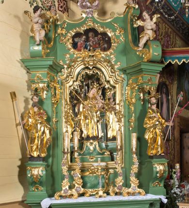 Zdjęcie nr 1: Nastawa ołtarzowa architektoniczna, jednoosiowa, jednokondygnacyjna ze zwieńczeniem. Mensa sarkofagowa, dekorowana na froncie dwiema płycinami w kształcie leżących prostokątów, ujętych po bokach i spiętych motywem ornamentalnym utworzonym z rocaille’a i liści.  
 Oś nastawy flankowana pilastrami przechodzącymi dołem w konsole i górą we fragmenty pełnego belkowania, o delikatnie wklęsło-wypukłej linii gzymsu. Zwieńczenie w formie wklęsło-wypukłej ujęte spływającymi na belkowanie dużymi wolutami, zamknięte stylizowanym gzymsem z ceowników i zwieńczone gołębicą Ducha Świętego na tle glorii, między główkami anielskimi, osadzone na obłoku. W polu środkowym pierwszej kondygnacji nisza z figurą Matki Boskiej Różańcowej wymiennie z obrazem ze sceną Zwiastowania ujęta profilowaną ramą w formie stojącego prostokąta zamkniętego łukiem półkolistym nadwieszonym z uskokiem, dekorowana fragmentami rocaille’ów. Na konsolach figury św. Joachima po lewej stronie i św. Józefa po prawej. W polu zwieńczenia obraz z przedstawieniem św. Rodziny ujęty ramą w formie trójlistnej, dekorowaną fragmentami rocaille'ów i flankowaną kwitnącymi gałązkami. Brzeg zwieńczenia i woluty zdobione taśmą i rocaille’ami, na wolutach para siedzących puttów, na zwieńczeniu uskrzydlone główki anielskie. 
Struktura polichromowana w kolorze zielonym, z marmoryzowanym cokołem i płycinami; ornamentyka i profile złocone i srebrzone.
