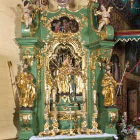 Zdjęcie nr 1: Nastawa ołtarzowa architektoniczna, jednoosiowa, jednokondygnacyjna ze zwieńczeniem. Mensa sarkofagowa, dekorowana na froncie dwiema płycinami w kształcie leżących prostokątów, ujętych po bokach i spiętych motywem ornamentalnym utworzonym z rocaille’a i liści.  
 Oś nastawy flankowana pilastrami przechodzącymi dołem w konsole i górą we fragmenty pełnego belkowania, o delikatnie wklęsło-wypukłej linii gzymsu. Zwieńczenie w formie wklęsło-wypukłej ujęte spływającymi na belkowanie dużymi wolutami, zamknięte stylizowanym gzymsem z ceowników i zwieńczone gołębicą Ducha Świętego na tle glorii, między główkami anielskimi, osadzone na obłoku. W polu środkowym pierwszej kondygnacji nisza z figurą Matki Boskiej Różańcowej wymiennie z obrazem ze sceną Zwiastowania ujęta profilowaną ramą w formie stojącego prostokąta zamkniętego łukiem półkolistym nadwieszonym z uskokiem, dekorowana fragmentami rocaille’ów. Na konsolach figury św. Joachima po lewej stronie i św. Józefa po prawej. W polu zwieńczenia obraz z przedstawieniem św. Rodziny ujęty ramą w formie trójlistnej, dekorowaną fragmentami rocaille'ów i flankowaną kwitnącymi gałązkami. Brzeg zwieńczenia i woluty zdobione taśmą i rocaille’ami, na wolutach para siedzących puttów, na zwieńczeniu uskrzydlone główki anielskie. 
Struktura polichromowana w kolorze zielonym, z marmoryzowanym cokołem i płycinami; ornamentyka i profile złocone i srebrzone.
