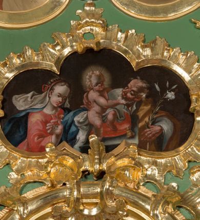 Zdjęcie nr 7: Nastawa ołtarzowa architektoniczna, jednoosiowa, jednokondygnacyjna ze zwieńczeniem. Mensa sarkofagowa, dekorowana na froncie dwiema płycinami w kształcie leżących prostokątów, ujętych po bokach i spiętych motywem ornamentalnym utworzonym z rocaille’a i liści.  
 Oś nastawy flankowana pilastrami przechodzącymi dołem w konsole i górą we fragmenty pełnego belkowania, o delikatnie wklęsło-wypukłej linii gzymsu. Zwieńczenie w formie wklęsło-wypukłej ujęte spływającymi na belkowanie dużymi wolutami, zamknięte stylizowanym gzymsem z ceowników i zwieńczone gołębicą Ducha Świętego na tle glorii, między główkami anielskimi, osadzone na obłoku. W polu środkowym pierwszej kondygnacji nisza z figurą Matki Boskiej Różańcowej wymiennie z obrazem ze sceną Zwiastowania ujęta profilowaną ramą w formie stojącego prostokąta zamkniętego łukiem półkolistym nadwieszonym z uskokiem, dekorowana fragmentami rocaille’ów. Na konsolach figury św. Joachima po lewej stronie i św. Józefa po prawej. W polu zwieńczenia obraz z przedstawieniem św. Rodziny ujęty ramą w formie trójlistnej, dekorowaną fragmentami rocaille'ów i flankowaną kwitnącymi gałązkami. Brzeg zwieńczenia i woluty zdobione taśmą i rocaille’ami, na wolutach para siedzących puttów, na zwieńczeniu uskrzydlone główki anielskie. 
Struktura polichromowana w kolorze zielonym, z marmoryzowanym cokołem i płycinami; ornamentyka i profile złocone i srebrzone.
