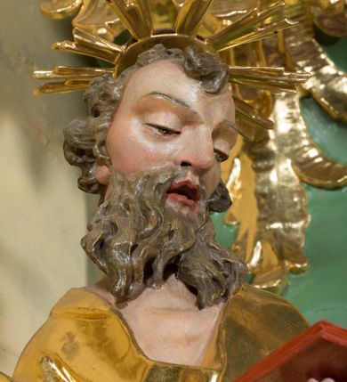 Zdjęcie nr 6: Rzeźba pełna, na cokole, ukazująca św. Joachima w całej postaci, w kontrapoście, frontalnie. Święty spogląda w dół, trzyma w lewej ręce otwartą książkę, w prawej dzierży łopatę pasterską. Ma owalną twarz o wąskich brwiach, dużych, migdałowatych oczach, dużym nosie i otwartych ustach, okoloną długą, rozdzielającą się na pół brodą i układającymi się w pukle włosami; nad głową nimb. Jest ubrany w długą suknię w dużym dekoltem, która podkreśla kształt ciała, łamiąc się grubymi fałdami. Na nogach ma sandały. Polichromia w partiach ciała naturalistyczna, szaty złocone, atrybuty złocone i srebrzone; krawędzie kart księgi w kolorze czerwonym. 