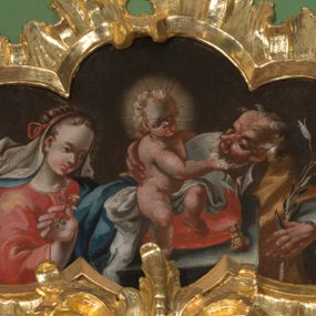 Zdjęcie nr 1: Obraz w kształcie czworoliścia z przedstawieniem Świętej Rodziny. Na środku sceny mały Jezus, widoczny w całej postaci, siedzi na poduszce umieszczonej na postumencie. Patrzy przed siebie, lewą ręką obejmuje św. Józefa, prawą bawi się jego brodą. Jest nagi, między nogami przechodzi mu jedynie biała tkanina. Ma podłużną twarz z wysokim czołem, szeroko rozstawionymi oczami, małym nosem i ustami. Jego jasne włosy kręcą się w loki; wokół głowy nimb. Święty Józef widoczny do pasa, stoi za postumentem. Patrzy na Dzieciątko, prawą ręką przytrzymuje jego plecy, w lewej, uniesionej trzyma kwiat lilii. Jest ubrany w białą, rozciętą pod szyją suknię i żółty płaszcz. Stojąca z lewej strony kompozycji Maria, również widoczna do pasa, spogląda na plecy Dzieciątka. W prawej, uniesionej ręce trzyma kwiat goździka. Ma owalną, młodą twarz, z wysokim czołem, drobnym nosem i ustami. Jest ubrana w czerwoną suknię i niebieski płaszcz. Ma misternie upięte włosy przewiązane czerwoną wstążką, spod niej w lewą stronę rozwiewa się biały welon. Wszystkie tkaniny gną się grubymi fałdami, tło jest jednolicie ciemnobrązowe. 