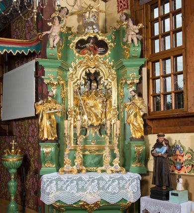 Zdjęcie nr 2: Nastawa ołtarzowa architektoniczna, jednoosiowa, jednokondygnacyjna ze zwieńczeniem. Mensa sarkofagowa, dekorowana na froncie dwiema płycinami w kształcie leżących prostokątów, ujętych po bokach i spiętych motywem ornamentalnym utworzonym z rocaille’a i liści. Oś nastawy flankowana pilastrami przechodzącymi dołem w konsole i górą we fragmenty pełnego belkowania, o delikatnie wklęsło-wypukłej linii gzymsu. Zwieńczenie w formie wklęsło-wypukłej ujęte spływającymi na belkowanie dużymi wolutami, zamknięte stylizowanym gzymsem z ceowników i zwieńczone wyobrażeniem oka Opatrzności, na tle glorii promienistej i obłoków. W polu środkowym pierwszej kondygnacji rzeźba ukazująca św. Mikołaja przesłaniana obrazem z przedstawieniem św. Antoniego Padewskiego adorującego Matkę Boską z Dzieciątkiem wykonanym w 1830 roku przez nowotarskiego malarza Tomasza Nankego, na zamówienie organisty Jakuba Pasigowskiego. Nisza ujęta profilowaną ramą w formie stojącego prostokąta zamkniętego łukiem półkolistym nadwieszonym z uskokiem, dekorowana fragmentami rocaille’ów. Na konsolach figury św. Jana Nepomucena po lewej stronie i św. Karola Boromeusza po prawej. W polu zwieńczenia obraz z przedstawieniem św. Agaty ujęty ramą w formie trójlistnej, dekorowaną fragmentami rocaille'ów i flankowaną kwitnącymi gałązkami. Brzeg zwieńczenia i woluty zdobione taśmą i rocaille'ami, na wolutach para siedzących puttów, na zwieńczeniu uskrzydlone główki anielskie. 
Struktura polichromowana w kolorze zielonym, z marmoryzowanym cokołem i płycinami; ornamentyka i profile złocone i srebrzone.

