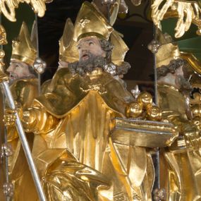 Zdjęcie nr 1: Rzeźba pełna, na cokole, ukazująca św. Mikołaja w całej postaci, w kontrapoście z ciałem skręconym lekko w prawą stronę. Święty wznosi wzrok nieznacznie do góry, w prawej ręce trzyma pastorał, lewą przytrzymuje opartą na biodrze, zamkniętą księgę, na której leżą trzy złote kule (jabłka). Ma podłużną twarz o wąskich brwiach, dużych, migdałowatych oczach, dużym nosie i otwartych ustach, okoloną długą, siwiejącą brodą i układającymi się w pukle włosami. Jest ubrany w strój biskupi: albę, dekorowaną szerokim pasem koronki rokietę oraz spiętą pod szyją kapę. Obszerne szaty opadają ku ziemi, gnąc się grubymi fałdami, część wywija się ponad prawym kolanem. Na głowie ma infułę, na nogach buty o ściętych czubkach. Polichromia w partiach ciała naturalistyczna, szaty złocone, atrybuty złocone i srebrzone. 