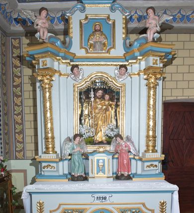 Zdjęcie nr 1: Nastawa ołtarzowa architektoniczna, ustawiona na jednym stopniu, jednoosiowa, jednokondygnacyjna ze zwieńczeniem. Ołtarz drewniany, prostopadłościenny, z drewnianą mensą i marmurowym portatylem. Antepedium w formie leżącego prostokąta, na niskim cokole, ujętego od góry profilowanym gzymsem, z płyciną w kształcie leżącego prostokąta o wklęsłych narożach w polu. Po bokach płycina flankowana płaskorzeźbionymi gałązkami lauru wyrastającymi z ośmiopłatkowego kwiatka, z równomiernie ułożonym rzędem listków po bokach. W polu płyciny ustawione obok siebie trzy mniejsze płyciny w profilowanych, złoconych ramach z płaskorzeźbioną dekoracją umieszczoną na niebieskim tle. W środkowej, okrągłej płycinie równoramienny krzyż o trójlistnych zakończeniach z odchodzącymi od środka wiązkami promieni. Płyciny po bokach dopasowane do środkowej jednym bokiem o wykroju wklęsłym i z wklęsłymi narożami na boku przeciwległym, z płaskorzeźbioną, stylizowaną wicią roślinną w polu. U góry antepedium malowany kartusz z datą „1890”. Tabernakulum w formie prostopadłościanu, na niskim cokole, o wypukłej ściance frontowej flankowanej po bokach dwiema kanelurami, z drzwiczkami w złoconej ramie, zdobionymi prostokątną, niebieską płyciną ze złoconym kielichem i hostią pośrodku, zamkniętego łukiem nadwieszonym, z gzymsem w formie dwóch wolut spiętych pośrodku akroterionem. Retabulum na niskim cokole, flankowane parą kolumn, podtrzymujących przerwane belkowanie. Kolumny ustawione na kwadratowych podstawach, z trzonem w dolnej części zdobionym opaską z rzędu sześciopłatkowych kwiatków ograniczoną od dołu i góry pierścieniami, powyżej trzon owinięty wicią złożoną z ukwieconej gałązki, kapitele kompozytowe. Kolumny dźwigają ustawione ukośnie imposty i profilowane belkowanie, nad którym ustawione ukośne woluty połączone ze zwieńczeniem. Na wolutach siedząca para aniołków. W polu środkowym nisza z rzeźbą św. Józefa z Dzieciątkiem, której ścianki złożone są z wielobocznych luster, z złoconymi, czteropłatkowymi kwiatkami na złączeniach. Nisza ujęta profilowaną ramą w formie stojącego prostokąta zamkniętego łukiem wklęsło-wypukłym z uskokami. Na zasuwie obraz z przedstawieniem stygmatyzacji św. Franciszka. Nad niszą, w narożach uskrzydlone główki aniołków. Zwieńczenie w kształcie kwadratu zamknięte od góry wydatnym gzymsem pośrodku i dwiema wolutami w narożach. W polu płycina w kształcie stojącego prostokąta o wklęsłych narożach, z płaskorzeźbą Najświętszego Serca Pana Jezusa. Rama płyciny złocona, profilowana. Struktura polichromowana na kolor błękitny, detale niebieskie, ornamentyka, kolumny i profilowania złocone i srebrzone. Na ołtarzu, po bokach tabernakulum ustawione dwie rzeźby aniołów.