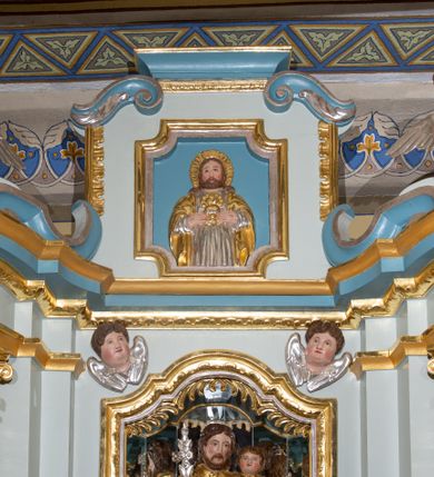 Zdjęcie nr 4: Nastawa ołtarzowa architektoniczna, ustawiona na jednym stopniu, jednoosiowa, jednokondygnacyjna ze zwieńczeniem. Ołtarz drewniany, prostopadłościenny, z drewnianą mensą i marmurowym portatylem. Antepedium w formie leżącego prostokąta, na niskim cokole, ujętego od góry profilowanym gzymsem, z płyciną w kształcie leżącego prostokąta o wklęsłych narożach w polu. Po bokach płycina flankowana płaskorzeźbionymi gałązkami lauru wyrastającymi z ośmiopłatkowego kwiatka, z równomiernie ułożonym rzędem listków po bokach. W polu płyciny ustawione obok siebie trzy mniejsze płyciny w profilowanych, złoconych ramach z płaskorzeźbioną dekoracją umieszczoną na niebieskim tle. W środkowej, okrągłej płycinie równoramienny krzyż o trójlistnych zakończeniach z odchodzącymi od środka wiązkami promieni. Płyciny po bokach dopasowane do środkowej jednym bokiem o wykroju wklęsłym i z wklęsłymi narożami na boku przeciwległym, z płaskorzeźbioną, stylizowaną wicią roślinną w polu. U góry antepedium malowany kartusz z datą „1890”. Tabernakulum w formie prostopadłościanu, na niskim cokole, o wypukłej ściance frontowej flankowanej po bokach dwiema kanelurami, z drzwiczkami w złoconej ramie, zdobionymi prostokątną, niebieską płyciną ze złoconym kielichem i hostią pośrodku, zamkniętego łukiem nadwieszonym, z gzymsem w formie dwóch wolut spiętych pośrodku akroterionem. Retabulum na niskim cokole, flankowane parą kolumn, podtrzymujących przerwane belkowanie. Kolumny ustawione na kwadratowych podstawach, z trzonem w dolnej części zdobionym opaską z rzędu sześciopłatkowych kwiatków ograniczoną od dołu i góry pierścieniami, powyżej trzon owinięty wicią złożoną z ukwieconej gałązki, kapitele kompozytowe. Kolumny dźwigają ustawione ukośnie imposty i profilowane belkowanie, nad którym ustawione ukośne woluty połączone ze zwieńczeniem. Na wolutach siedząca para aniołków. W polu środkowym nisza z rzeźbą św. Józefa z Dzieciątkiem, której ścianki złożone są z wielobocznych luster, z złoconymi, czteropłatkowymi kwiatkami na złączeniach. Nisza ujęta profilowaną ramą w formie stojącego prostokąta zamkniętego łukiem wklęsło-wypukłym z uskokami. Na zasuwie obraz z przedstawieniem stygmatyzacji św. Franciszka. Nad niszą, w narożach uskrzydlone główki aniołków. Zwieńczenie w kształcie kwadratu zamknięte od góry wydatnym gzymsem pośrodku i dwiema wolutami w narożach. W polu płycina w kształcie stojącego prostokąta o wklęsłych narożach, z płaskorzeźbą Najświętszego Serca Pana Jezusa. Rama płyciny złocona, profilowana. Struktura polichromowana na kolor błękitny, detale niebieskie, ornamentyka, kolumny i profilowania złocone i srebrzone. Na ołtarzu, po bokach tabernakulum ustawione dwie rzeźby aniołów.