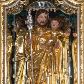 Zdjęcie nr 1: Rzeźba pełna, ustawiona na prostokątnym cokole. Święty Józef ukazany frontalnie, z Dzieciątkiem na lewym ręku, z różdżką Jessego w prawej ręce. Jest ubrany w długą suknię z długimi rękawami, przepasaną sznurkiem oraz długi płaszcz spięty pod szyją, z prawym końcem zarzuconym na lewe przedramię, na stopach sandały. Ma podłużną, okoloną brodą twarz z długim, wąskim nosem i małymi oczami. Włosy brązowe, średniej długości, opadają na plecy. Dzieciątko zostało ukazane frontalnie, z rozpostartymi szeroko rękami, z lewą nogą założoną na prawą. Jest ubrane w długą sukienkę z długimi rękawami, przepasaną w pasie sznurkiem. Ma okrągłą twarz, z rumieńcami na pełnych policzkach i małymi, czerwonymi ustami oraz krótkim, szerokim nosem; włosy krótkie, falowane. Polichromia w partiach ciała naturalistyczna, szaty złocone, atrybut srebrzony.