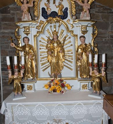 Zdjęcie nr 4: Nastawa ołtarzowa architektoniczna, jednoosiowa, jednokondygnacyjna ze zwieńczeniem. Ołtarz drewniany, prostopadłościenny, z drewnianą mensą. Antepedium w formie leżącego prostokąta obwiedzione profilem, z monogramem maryjnym po środku. Retabulum na niskim cokole, flankowane parą pilastrów przechodzących dołem w cokoły dla figur św. Wincentego Ferreriusza po lewej stronie i św. Jacka po prawej i konsole podtrzymujące fragmenty belkowania górą. Po dwóch stronach ażurowe uszaki utworzone z wici akantowej. Na konsolach umieszczono siedzące na chmurach aniołki wskazujące na Trójcę Świętą w zwieńczeniu. W dolnej części sceny stoją naprzeciwko siebie Chrystus oraz Bóg Ojciec stąpający po granatowych chmurach, ponad nimi unosi się gołębica Ducha Świętego na tle glorii promienistej, otoczona obłokami. Zwieńczenie zamknięte spływami wolutowymi dekorowanymi liśćmi. Nisza ujęta profilowaną ramą w formie stojącego prostokąta zamkniętego łukiem wklęsło-wypukłym z uskokami spiętą u góry ornamentem rocaille’owym. W niszy rzeźba Matki Boskiej Niepokalanie Poczętej. Struktura polichromowana na kolor biały, detale i ornamentyka złocone i srebrzone.  