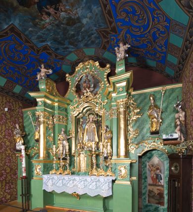 Zdjęcie nr 40: Nastawa ołtarzowa architektoniczna, jednoosiowa, jednokondygnacyjna ze zwieńczeniem oraz bramkami. Mensa sarkofagowa, dekorowana na froncie rokokowym kartuszem zawierającym datę odnowienia kościoła – 1869. Na niej tabernakulum w formie drewnianej skrzynki, o wklęsło-wypukłej ściance frontowej, flankowanej przez ukośnie dostawioną parę pilastrów na cokołach o trzonach w formie spływów wolutowych, dźwigających imposty oraz gzyms wyłamujący się w centrum w formę wspornika stanowiącego tron wystawienia. Całość ujęta ornamentalnymi spływami ustawionymi na cokole z prześwitami wypełnionymi kratką z krzyżykami. Drzwiczki w formie stojącego prostokąta zamkniętego łukiem półkolistym nadwieszonym, dekorowanym rocaille'em; w polu na fakturowanym tle płaskorzeźbione przedstawienie kielicha z hostią w glorii. 
Nastawa ołtarzowa ustawiona na dwustrefowym cokole, zryzalitowanym przy brzegach; ujęta wiązką pilastrów i stojącą przed nimi parą kolumn o kapitelach kompozytowych, dźwigających fragmenty pełnego belkowania, o delikatnie wklęsło-wypukłej linii gzymsu. Zwieńczenie w formie wklęsło-wypukłej, ujęte spływającymi na belkowanie dużymi wolutami, zamknięte stylizowanym gzymsem w formie łuku odcinkowego nadwieszonego z uskokiem. W polu środkowym pierwszej kondygnacji nisza z figurą Matki Boskiej Różańcowej wymiennie z figurą św. Sebastiana i obrazem z przedstawieniem męczeństwa św. Sebastiana, ujęta profilowaną ramą w formie stojącego prostokąta zamkniętego łukiem półkolistym nadwieszonym z uskokiem, dekorowana fragmentami rocaille'ów oraz zwieńczona ażurową konstrukcją utworzoną z rocaille'ów. Przed pilastrami rocaille’owe wsporniki z figurami św. Piotra i św. Pawła. W polu zwieńczenia obraz z przedstawieniem św. Floriana ujęty ramą w formie zbliżonej do koła z wpisanym kwadratem, dekorowaną fragmentami rocaille'ów i flankowaną zwisami utworzonymi z ulistnionych gałązek. Brzeg zwieńczenia i woluty zdobione rocaille’ową falbaną, na wolutach para siedzących puttów trzymających róże. Bramki ujęte od zewnątrz parą opilastrowanych filarów o trzonach dekorowanych rocaille'em, na których stoją figury św. Jana Ewangelisty po lewej i św. Jana Chrzciciela po prawej stronie. Przejścia w formie stojącego prostokąta zamkniętego łukiem odcinkowym nadwieszonym, z drzwiami o tym samym kształcie dekorowanymi płyciną z czterema uszakami, zakończoną trójkątnie z malowanymi na drewnie przedstawieniami Archanioła Michała po lewej i Archanioła Rafała po prawej stronie. Bramki zamknięte stylizowanym łukiem odcinkowym nadwieszonym dekorowanym rocaille'em zwieńczonym wspornikiem na rzeźby św. Stanisława i św. Wojciecha. Powyżej bramek proste ścianki zamknięte profilowanym gzymsem, wypełniające całą szerokość prezbiterium. 
Struktura polichromowana w kolorze zielonym, z marmoryzowanymi detalami i ściankami osi zewnętrznych; ornamentyka, profile i kolumny złocone i srebrzone.
