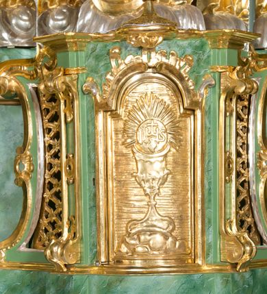 Zdjęcie nr 32: Nastawa ołtarzowa architektoniczna, jednoosiowa, jednokondygnacyjna ze zwieńczeniem oraz bramkami. Mensa sarkofagowa, dekorowana na froncie rokokowym kartuszem zawierającym datę odnowienia kościoła – 1869. Na niej tabernakulum w formie drewnianej skrzynki, o wklęsło-wypukłej ściance frontowej, flankowanej przez ukośnie dostawioną parę pilastrów na cokołach o trzonach w formie spływów wolutowych, dźwigających imposty oraz gzyms wyłamujący się w centrum w formę wspornika stanowiącego tron wystawienia. Całość ujęta ornamentalnymi spływami ustawionymi na cokole z prześwitami wypełnionymi kratką z krzyżykami. Drzwiczki w formie stojącego prostokąta zamkniętego łukiem półkolistym nadwieszonym, dekorowanym rocaille'em; w polu na fakturowanym tle płaskorzeźbione przedstawienie kielicha z hostią w glorii. 
Nastawa ołtarzowa ustawiona na dwustrefowym cokole, zryzalitowanym przy brzegach; ujęta wiązką pilastrów i stojącą przed nimi parą kolumn o kapitelach kompozytowych, dźwigających fragmenty pełnego belkowania, o delikatnie wklęsło-wypukłej linii gzymsu. Zwieńczenie w formie wklęsło-wypukłej, ujęte spływającymi na belkowanie dużymi wolutami, zamknięte stylizowanym gzymsem w formie łuku odcinkowego nadwieszonego z uskokiem. W polu środkowym pierwszej kondygnacji nisza z figurą Matki Boskiej Różańcowej wymiennie z figurą św. Sebastiana i obrazem z przedstawieniem męczeństwa św. Sebastiana, ujęta profilowaną ramą w formie stojącego prostokąta zamkniętego łukiem półkolistym nadwieszonym z uskokiem, dekorowana fragmentami rocaille'ów oraz zwieńczona ażurową konstrukcją utworzoną z rocaille'ów. Przed pilastrami rocaille’owe wsporniki z figurami św. Piotra i św. Pawła. W polu zwieńczenia obraz z przedstawieniem św. Floriana ujęty ramą w formie zbliżonej do koła z wpisanym kwadratem, dekorowaną fragmentami rocaille'ów i flankowaną zwisami utworzonymi z ulistnionych gałązek. Brzeg zwieńczenia i woluty zdobione rocaille’ową falbaną, na wolutach para siedzących puttów trzymających róże. Bramki ujęte od zewnątrz parą opilastrowanych filarów o trzonach dekorowanych rocaille'em, na których stoją figury św. Jana Ewangelisty po lewej i św. Jana Chrzciciela po prawej stronie. Przejścia w formie stojącego prostokąta zamkniętego łukiem odcinkowym nadwieszonym, z drzwiami o tym samym kształcie dekorowanymi płyciną z czterema uszakami, zakończoną trójkątnie z malowanymi na drewnie przedstawieniami Archanioła Michała po lewej i Archanioła Rafała po prawej stronie. Bramki zamknięte stylizowanym łukiem odcinkowym nadwieszonym dekorowanym rocaille'em zwieńczonym wspornikiem na rzeźby św. Stanisława i św. Wojciecha. Powyżej bramek proste ścianki zamknięte profilowanym gzymsem, wypełniające całą szerokość prezbiterium. 
Struktura polichromowana w kolorze zielonym, z marmoryzowanymi detalami i ściankami osi zewnętrznych; ornamentyka, profile i kolumny złocone i srebrzone.
