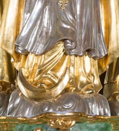 Zdjęcie nr 4: Rzeźba pełna, Madonna ukazana w całej postaci, zwrócona frontalnie, stojąca na chmurach, z księżycem pod prawą stopą, dłońmi złożonymi do modlitwy i głową lekko uniesioną do góry. Ma wydłużoną twarz o pełnych policzkach, oczy niewielkie, zwrócone ku górze, prosty nos, usta małe i pełne. Długie, gęste, falowane włosy opadają jej na plecy. Na głowie korona otwarta, wokół niej nimb złożony z 12 gwiazd. Jest ubrana w długą suknię spodnią o wąskich rękawach i krótszą wierzchnią o szerokich rękawach, obficie drapowaną w drobne fałdy, brzegi stroju rozwiane. Na piersi ma zawieszony różaniec, którego koniec sięga wysokości kolan. Postać okrywa płaszcz zapięty pod szyją i opadający na ramiona i plecy, z odwiniętym brzegiem. Polichromia naturalistyczna w odsłoniętych partiach ciała, szaty i atrybuty złocone i srebrzone.