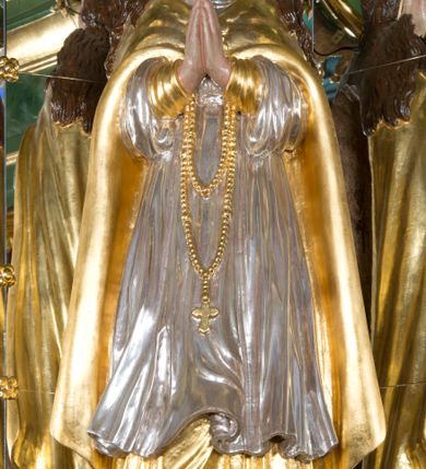 Zdjęcie nr 3: Rzeźba pełna, Madonna ukazana w całej postaci, zwrócona frontalnie, stojąca na chmurach, z księżycem pod prawą stopą, dłońmi złożonymi do modlitwy i głową lekko uniesioną do góry. Ma wydłużoną twarz o pełnych policzkach, oczy niewielkie, zwrócone ku górze, prosty nos, usta małe i pełne. Długie, gęste, falowane włosy opadają jej na plecy. Na głowie korona otwarta, wokół niej nimb złożony z 12 gwiazd. Jest ubrana w długą suknię spodnią o wąskich rękawach i krótszą wierzchnią o szerokich rękawach, obficie drapowaną w drobne fałdy, brzegi stroju rozwiane. Na piersi ma zawieszony różaniec, którego koniec sięga wysokości kolan. Postać okrywa płaszcz zapięty pod szyją i opadający na ramiona i plecy, z odwiniętym brzegiem. Polichromia naturalistyczna w odsłoniętych partiach ciała, szaty i atrybuty złocone i srebrzone.