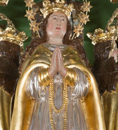 Zdjęcie nr 2: Rzeźba pełna, Madonna ukazana w całej postaci, zwrócona frontalnie, stojąca na chmurach, z księżycem pod prawą stopą, dłońmi złożonymi do modlitwy i głową lekko uniesioną do góry. Ma wydłużoną twarz o pełnych policzkach, oczy niewielkie, zwrócone ku górze, prosty nos, usta małe i pełne. Długie, gęste, falowane włosy opadają jej na plecy. Na głowie korona otwarta, wokół niej nimb złożony z 12 gwiazd. Jest ubrana w długą suknię spodnią o wąskich rękawach i krótszą wierzchnią o szerokich rękawach, obficie drapowaną w drobne fałdy, brzegi stroju rozwiane. Na piersi ma zawieszony różaniec, którego koniec sięga wysokości kolan. Postać okrywa płaszcz zapięty pod szyją i opadający na ramiona i plecy, z odwiniętym brzegiem. Polichromia naturalistyczna w odsłoniętych partiach ciała, szaty i atrybuty złocone i srebrzone.