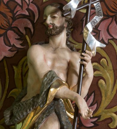 Zdjęcie nr 1: Figura ukazująca św. Jana Chrzciciela w całej postaci, w kontrapoście, sylwetka delikatnie wygięta w lewo, w skręcie. Święty w lewej ręce trzyma długie drzewce zakończone krzyżem z przewiązaną banderolą z napisem „ECCE AGNUS DEI”, prawą rękę silnie wysuwa w lewą stronę. Twarz szczupła o dużych szeroko rozstawionych i migdałowatych oczach z wyraźnie rzeźbionymi powiekami, dużym zaoblonym nosem; okolona zarostem oraz włosami do ramion w postaci silnie przylegających do głowy, falujących pukli. Święty ma narzucony płaszcz ze skóry ze złoconym podbiciem, zawiązany na prawym przedramieniu i w partii bioder, odsłaniający lewe udo. U stóp figury rzeźba leżącego baranka z głową skierowaną ku górze. Polichromia partii ciała naturalistyczna, detal złocony i srebrzony. 