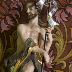 Zdjęcie nr 1: Figura ukazująca św. Jana Chrzciciela w całej postaci, w kontrapoście, sylwetka delikatnie wygięta w lewo, w skręcie. Święty w lewej ręce trzyma długie drzewce zakończone krzyżem z przewiązaną banderolą z napisem „ECCE AGNUS DEI”, prawą rękę silnie wysuwa w lewą stronę. Twarz szczupła o dużych szeroko rozstawionych i migdałowatych oczach z wyraźnie rzeźbionymi powiekami, dużym zaoblonym nosem; okolona zarostem oraz włosami do ramion w postaci silnie przylegających do głowy, falujących pukli. Święty ma narzucony płaszcz ze skóry ze złoconym podbiciem, zawiązany na prawym przedramieniu i w partii bioder, odsłaniający lewe udo. U stóp figury rzeźba leżącego baranka z głową skierowaną ku górze. Polichromia partii ciała naturalistyczna, detal złocony i srebrzony. 