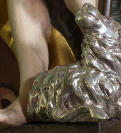 Zdjęcie nr 5: Figura ukazująca św. Jana Chrzciciela w całej postaci, w kontrapoście, sylwetka delikatnie wygięta w lewo, w skręcie. Święty w lewej ręce trzyma długie drzewce zakończone krzyżem z przewiązaną banderolą z napisem „ECCE AGNUS DEI”, prawą rękę silnie wysuwa w lewą stronę. Twarz szczupła o dużych szeroko rozstawionych i migdałowatych oczach z wyraźnie rzeźbionymi powiekami, dużym zaoblonym nosem; okolona zarostem oraz włosami do ramion w postaci silnie przylegających do głowy, falujących pukli. Święty ma narzucony płaszcz ze skóry ze złoconym podbiciem, zawiązany na prawym przedramieniu i w partii bioder, odsłaniający lewe udo. U stóp figury rzeźba leżącego baranka z głową skierowaną ku górze. Polichromia partii ciała naturalistyczna, detal złocony i srebrzony. 