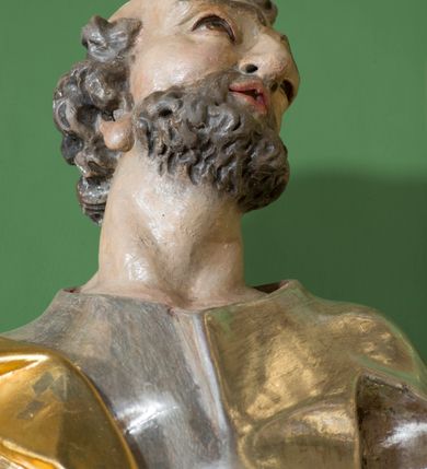 Zdjęcie nr 4: Rzeźba z przedstawieniem św. Piotra w całej postaci. Figura zwrócona frontalnie, w kontrapoście, sylwetka esowato wygięta; w lewej wyciągniętej w bok ręce trzyma klucze, prawą podtrzymuje na biodrze księgę. Głowę ma skierowaną w lewo, lekko uniesioną;  twarz szczupłą z wysokim czołem, o wyraźnie podkreślonych łukach brwiowych, nosie i kościach policzkowych, usta rozchylone. Twarz jest okolona krótkim kręconym zarostem oraz krótkimi silnie skręconymi włosami. Święty jest ubrany w długą, przylegającą do ciała tunikę oraz płaszcz przewiązany diagonalnie z prawego ramienia przez tors, podtrzymywany na wstędze. Polichromia naturalistyczna w odsłoniętych partiach ciała, szaty i atrybuty złocone i srebrzone.