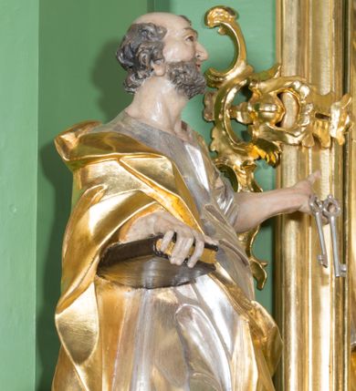 Zdjęcie nr 1: Rzeźba z przedstawieniem św. Piotra w całej postaci. Figura zwrócona frontalnie, w kontrapoście, sylwetka esowato wygięta; w lewej wyciągniętej w bok ręce trzyma klucze, prawą podtrzymuje na biodrze księgę. Głowę ma skierowaną w lewo, lekko uniesioną;  twarz szczupłą z wysokim czołem, o wyraźnie podkreślonych łukach brwiowych, nosie i kościach policzkowych, usta rozchylone. Twarz jest okolona krótkim kręconym zarostem oraz krótkimi silnie skręconymi włosami. Święty jest ubrany w długą, przylegającą do ciała tunikę oraz płaszcz przewiązany diagonalnie z prawego ramienia przez tors, podtrzymywany na wstędze. Polichromia naturalistyczna w odsłoniętych partiach ciała, szaty i atrybuty złocone i srebrzone.