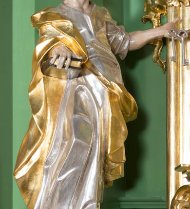 Zdjęcie nr 2: Rzeźba z przedstawieniem św. Piotra w całej postaci. Figura zwrócona frontalnie, w kontrapoście, sylwetka esowato wygięta; w lewej wyciągniętej w bok ręce trzyma klucze, prawą podtrzymuje na biodrze księgę. Głowę ma skierowaną w lewo, lekko uniesioną;  twarz szczupłą z wysokim czołem, o wyraźnie podkreślonych łukach brwiowych, nosie i kościach policzkowych, usta rozchylone. Twarz jest okolona krótkim kręconym zarostem oraz krótkimi silnie skręconymi włosami. Święty jest ubrany w długą, przylegającą do ciała tunikę oraz płaszcz przewiązany diagonalnie z prawego ramienia przez tors, podtrzymywany na wstędze. Polichromia naturalistyczna w odsłoniętych partiach ciała, szaty i atrybuty złocone i srebrzone.