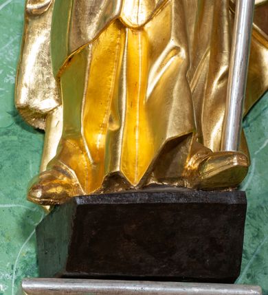 Zdjęcie nr 9: Rzeźba ukazująca św. Stanisława w całej postaci. Figura ustawiona frontalnie, w kontrapoście, łukowato przechylona w lewo; w lewej ręce trzyma pastorał, prawa ugięta, wyciągnięta przed siebie. Twarz kwadratowa o silnie zaznaczonych liniach łuków brwiowych i głęboko rzeźbionych powiekach, dużych oczach i nosie oraz małych, rozchylonych ustach, okolona krótkimi, silnie skręconymi włosami. Święty ubrany jest w złoconą albę, srebrzoną rokietę oraz złoconą kapę zapiętą na piersi, opadającą na ramiona, z fragmentem tkaniny zarzuconym na lewą nogę. Polichromia naturalistyczna w odsłoniętych partiach ciała, szaty i atrybuty złocone i srebrzone.