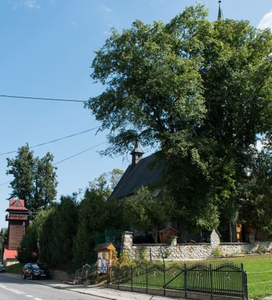 Zdjęcie nr 16: Kościół św. Elżbiety Węgierskiej w Trybszu usytuowany jest w centrum wsi na południe od drogi prowadzącej z Łapsz Wyżnych do Nowego Targu. Teren przykościelny jest otoczony od południa drewnianym ogrodzenie z murowanymi słupkami i kamienną podmurówką, z pozostałych stron mur z polnych kamieni, nakryty daszkiem cementowym. Główne wejście na teren przykościelny od północy, od zachodu bramka prowadząca do nowego kościoła, od południa furtka na cmentarz. Od zachodu główne wejście flankowane słupkami. Na placu przykościelnym stara lipa, w niej krucyfiks w kapliczkowej, szafkowej oprawie. W zachodniej części sztuczna grota, murowana z polnych kamieni z figurą Matki Boskiej z Lourdes. 

Kościół jest orientowany, drewniany o konstrukcji zrębowej, jednonawowy z wydłużonym prezbiterium zamkniętym trójbocznie, z kruchtą od południa i pierwotnie z zakrystią od północy i wieżą od zachodu. Wnętrze nakryte pułapem, w nawie z zaskrzynieniami, wiązanie nawy oparte nie na ścianach lecz na belkach podciągowych, których jeden koniec jest w ścianie tęczy, drugi zaś w czołowej ścianie nawy. Na zachodniej ścianie nawy chór muzyczny wsparty na dwóch filarach. Wnętrze oświetlają umieszczone w południowej ścianie trzy okna (dwa w prezbiterium i jedno w nawie). Ściany i stropy pokryte polichromią. Do kościoła prowadzi główne wejście od strony zachodniej oraz jedno przez kruchtę od południa. Dach o jednej kalenicy, gontowy, na środku drewniana sygnaturka, nakryta kopułką. Portal do zakrystii o wykroju w tzw. ośli grzbiet. 

