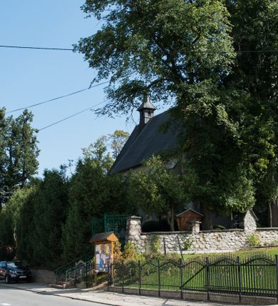 Zdjęcie nr 15: Kościół św. Elżbiety Węgierskiej w Trybszu usytuowany jest w centrum wsi na południe od drogi prowadzącej z Łapsz Wyżnych do Nowego Targu. Teren przykościelny jest otoczony od południa drewnianym ogrodzenie z murowanymi słupkami i kamienną podmurówką, z pozostałych stron mur z polnych kamieni, nakryty daszkiem cementowym. Główne wejście na teren przykościelny od północy, od zachodu bramka prowadząca do nowego kościoła, od południa furtka na cmentarz. Od zachodu główne wejście flankowane słupkami. Na placu przykościelnym stara lipa, w niej krucyfiks w kapliczkowej, szafkowej oprawie. W zachodniej części sztuczna grota, murowana z polnych kamieni z figurą Matki Boskiej z Lourdes. 

Kościół jest orientowany, drewniany o konstrukcji zrębowej, jednonawowy z wydłużonym prezbiterium zamkniętym trójbocznie, z kruchtą od południa i pierwotnie z zakrystią od północy i wieżą od zachodu. Wnętrze nakryte pułapem, w nawie z zaskrzynieniami, wiązanie nawy oparte nie na ścianach lecz na belkach podciągowych, których jeden koniec jest w ścianie tęczy, drugi zaś w czołowej ścianie nawy. Na zachodniej ścianie nawy chór muzyczny wsparty na dwóch filarach. Wnętrze oświetlają umieszczone w południowej ścianie trzy okna (dwa w prezbiterium i jedno w nawie). Ściany i stropy pokryte polichromią. Do kościoła prowadzi główne wejście od strony zachodniej oraz jedno przez kruchtę od południa. Dach o jednej kalenicy, gontowy, na środku drewniana sygnaturka, nakryta kopułką. Portal do zakrystii o wykroju w tzw. ośli grzbiet. 

